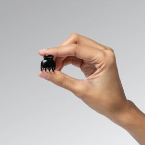 Hand holding a Black Micro Cloud hair clip between 2 fingers against a gray background