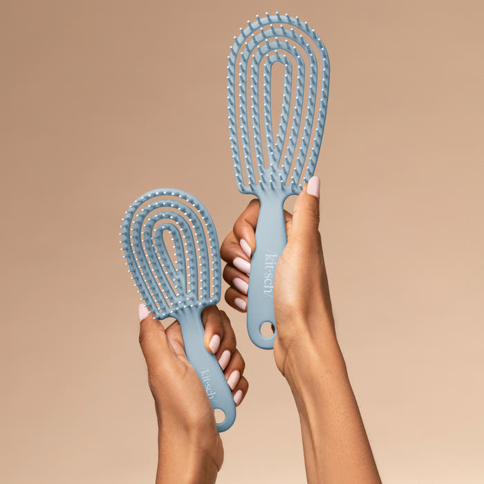Hand holding the Kitsch Haze Blue Detangling Flexi Brush Mini showing travel-friendly size