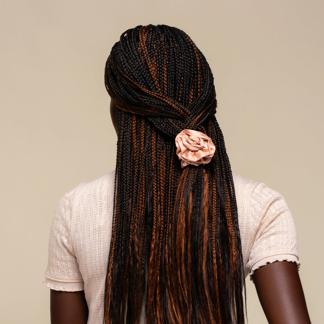 Person with microbraids styled with the Terracotta Rosette Ruched Satin Scrunchie on a plain beige background