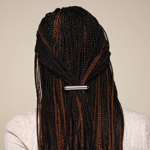 Person with micro braids featuring black and brown colors secured with a kitsch silver hair clip on a beige background