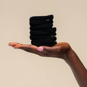 Hand holding a stack of kitsch ribbed black hair ties against a beige background