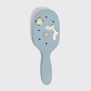 Decorative hairbrush with floral and bow designs on a light gray background