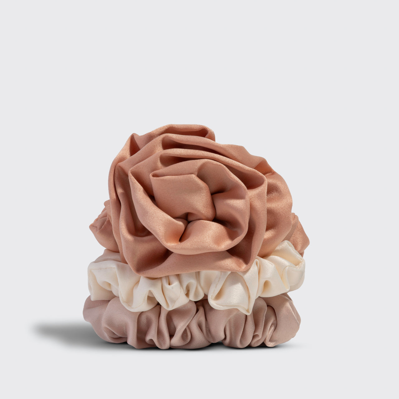 A terracotta rosette scrunchie stacked on 2 cream and beige scrunchies on a light gray background